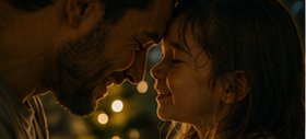 Pai e filha de testas encostadas, sorrindo, em luz dourada